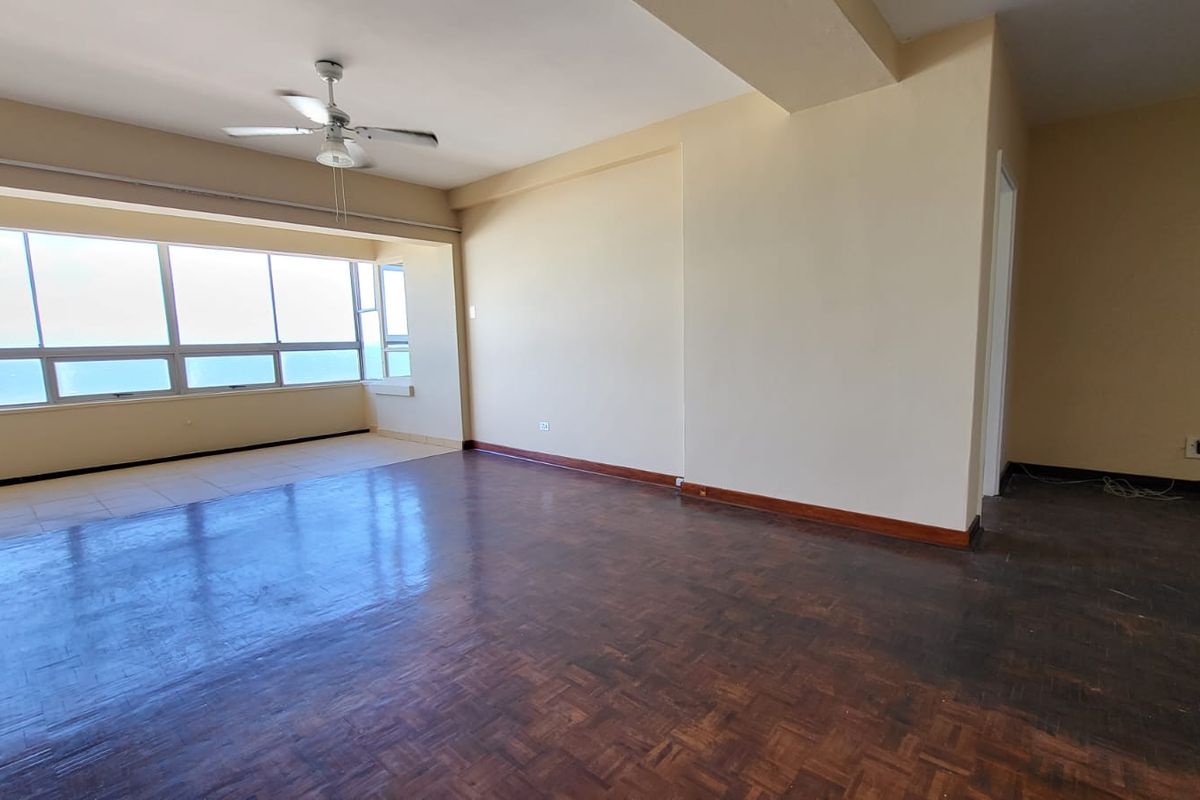 Spacious, empty living area featuring original parquet flooring, a ceiling fan, and expansive windows offering natural light and views.