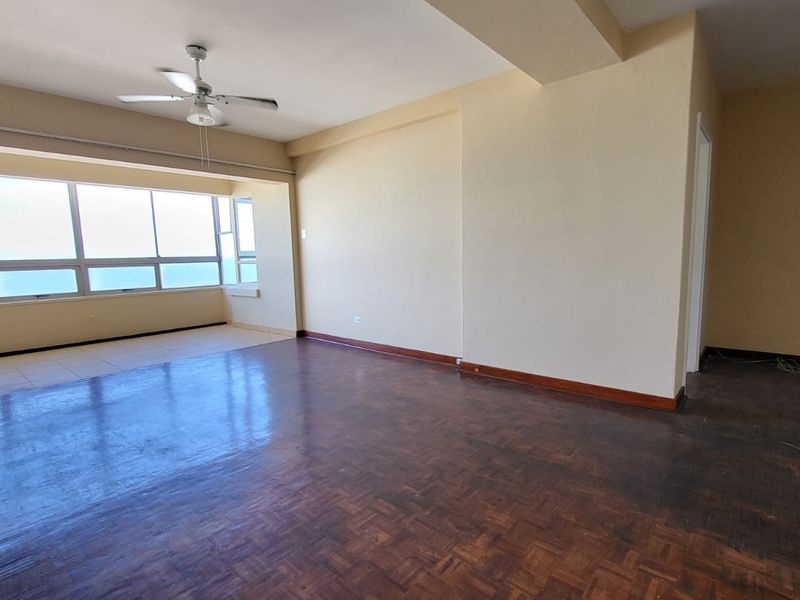 Spacious, empty living area featuring original parquet flooring, a ceiling fan, and expansive windows offering natural light and views.