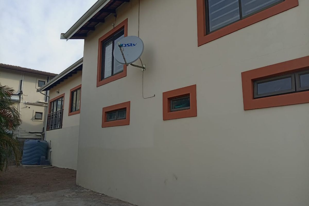 A view of the rear exterior wall of the house, featuring painted trim, window frames, and a mounted satellite dish.