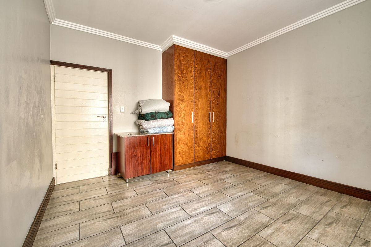 A bedroom featuring wood-look tile flooring, built-in wooden cabinetry, and crown molding, offering a functional space with neutral wall tones.