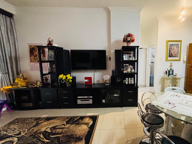 A living room area featuring neutral tiled flooring and coved ceiling detailing, providing a functional space for relaxation and dining.