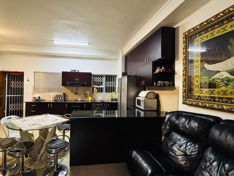 Open-plan living area featuring a kitchen with dark cabinetry, granite countertops, and a breakfast bar, seamlessly connected to the dining and lounge space.