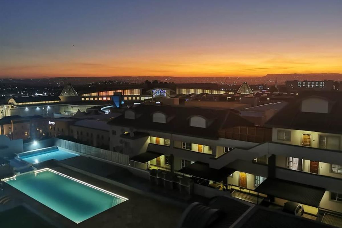 Aerial view of an apartment complex at dusk, featuring a swimming pool and surrounding residential buildings with sunset skyline views.