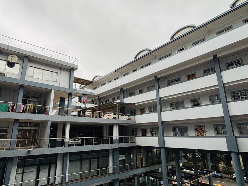 Exterior view of a multi-story apartment complex featuring tiered balconies, concrete structural pillars, and integrated covered parking levels.