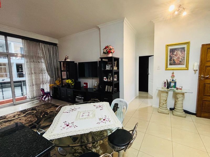 Open-plan living and dining area featuring neutral tiled flooring, cove ceiling detailing, and large sliding glass doors providing access to the balcony.