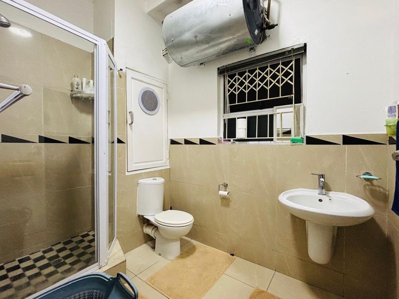 A functional bathroom featuring a shower enclosure, pedestal basin, toilet, and an exposed electric water heater unit.