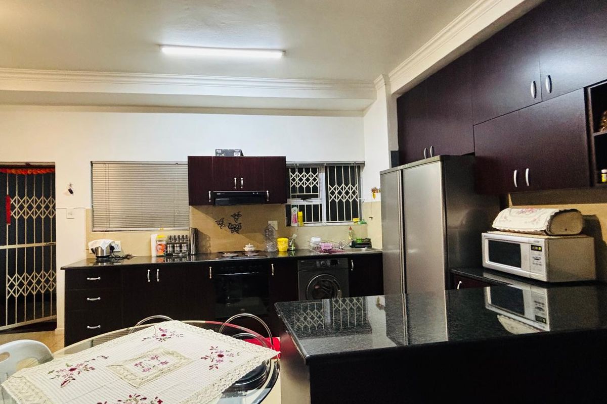 A functional kitchen featuring dark wood cabinetry, granite countertops, built-in oven, and an extractor fan, with security features on windows and doors.