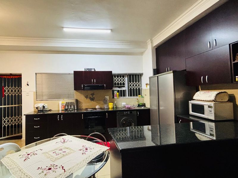A functional kitchen featuring dark wood cabinetry, granite countertops, built-in oven, and an extractor fan, with security features on windows and doors.
