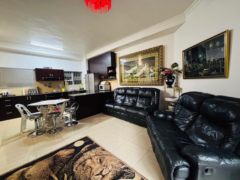 Open-plan living area featuring a kitchen with dark cabinetry and a breakfast island, seamlessly flowing into the main living space with tiled flooring.