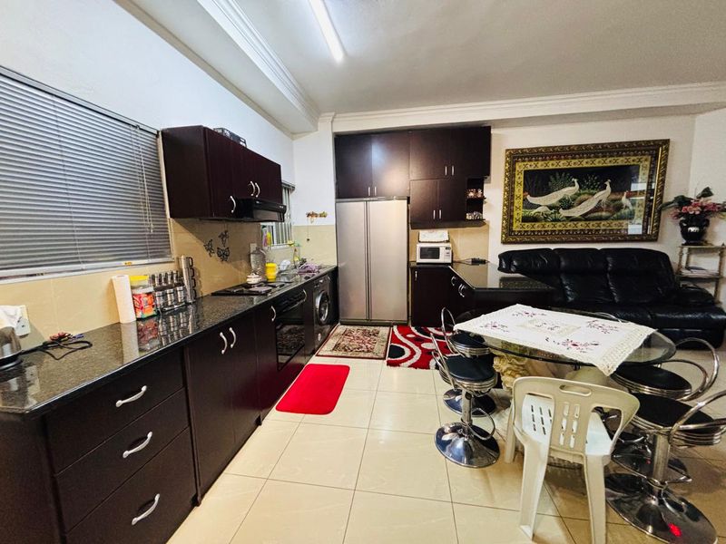 Open-plan kitchen and living area featuring dark wood cabinetry, granite countertops, built-in appliances, and tiled flooring throughout.