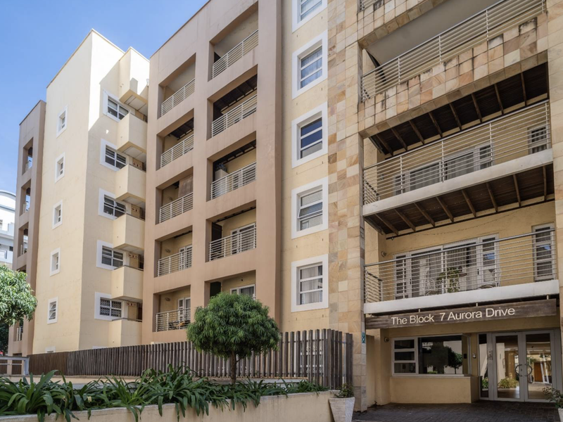 Front elevation of The Block 7 Aurora Drive apartment building, featuring modern stone cladding, private balconies with metal railings, and a secure glass entrance.