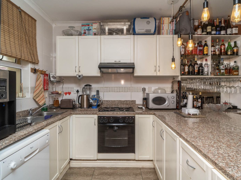 A functional kitchen featuring granite countertops, built-in cabinetry, a gas hob with extractor fan, and a tiled backsplash.