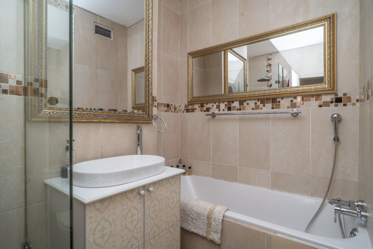 A compact bathroom featuring a vessel sink on a vanity cabinet, a bathtub with a shower mixer, and decorative wall tiling.
