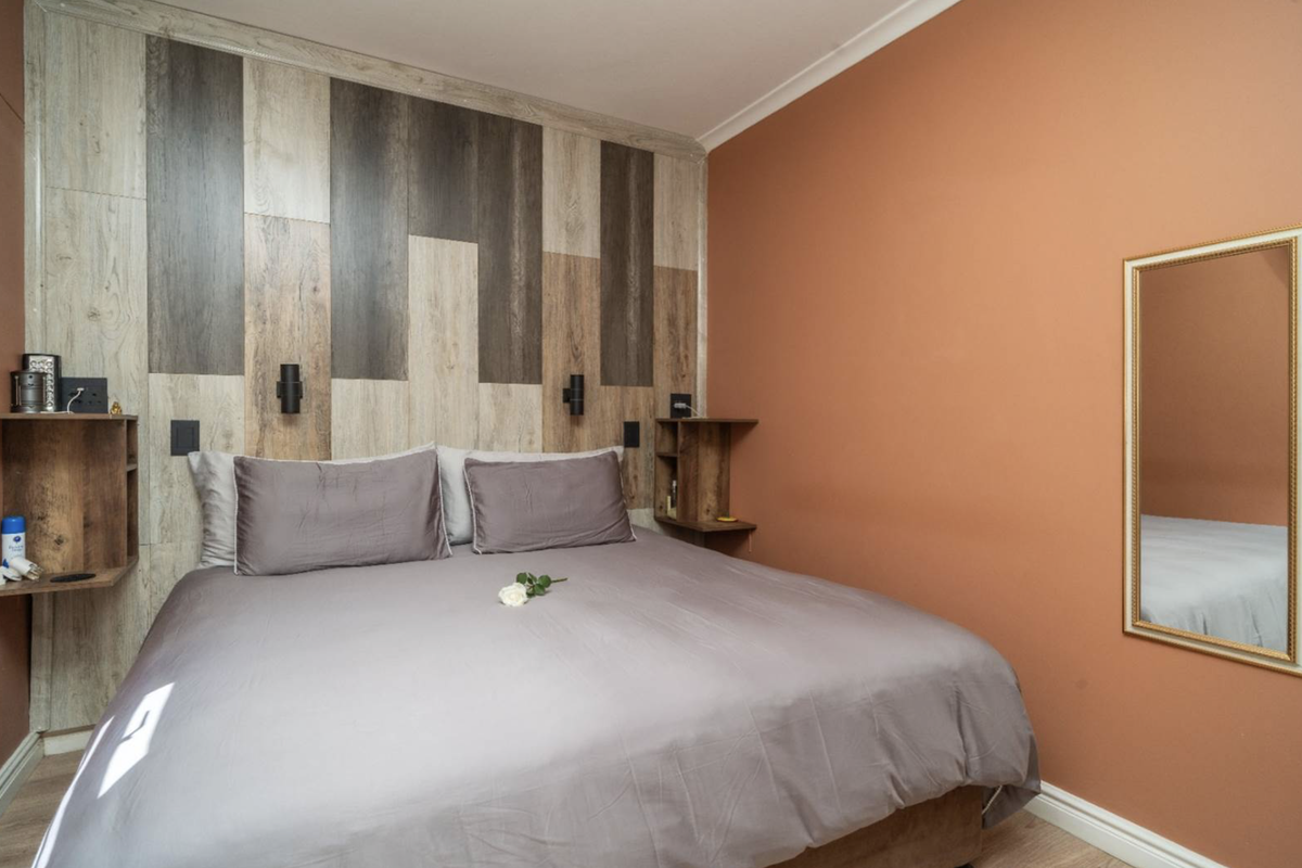 A cozy bedroom featuring a wood-look accent wall, built-in bedside shelving, and wall-mounted lighting, finished with warm-toned paint.