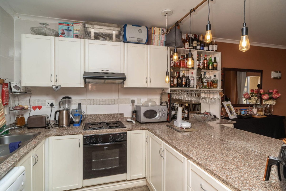 A functional kitchen featuring granite countertops, built-in cabinetry, an integrated oven with hob, and a tiled backsplash with modern pendant lighting.