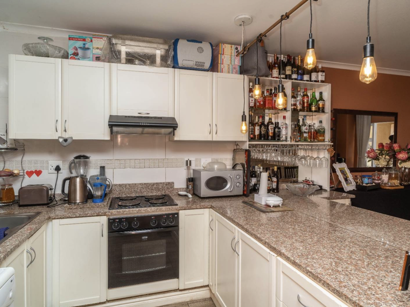 A functional kitchen featuring granite countertops, built-in cabinetry, an integrated oven with hob, and a tiled backsplash with modern pendant lighting.