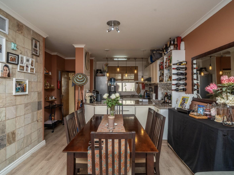 Open-plan dining and kitchen area featuring a stone-clad feature wall, laminate flooring, and functional cabinetry with granite countertops.