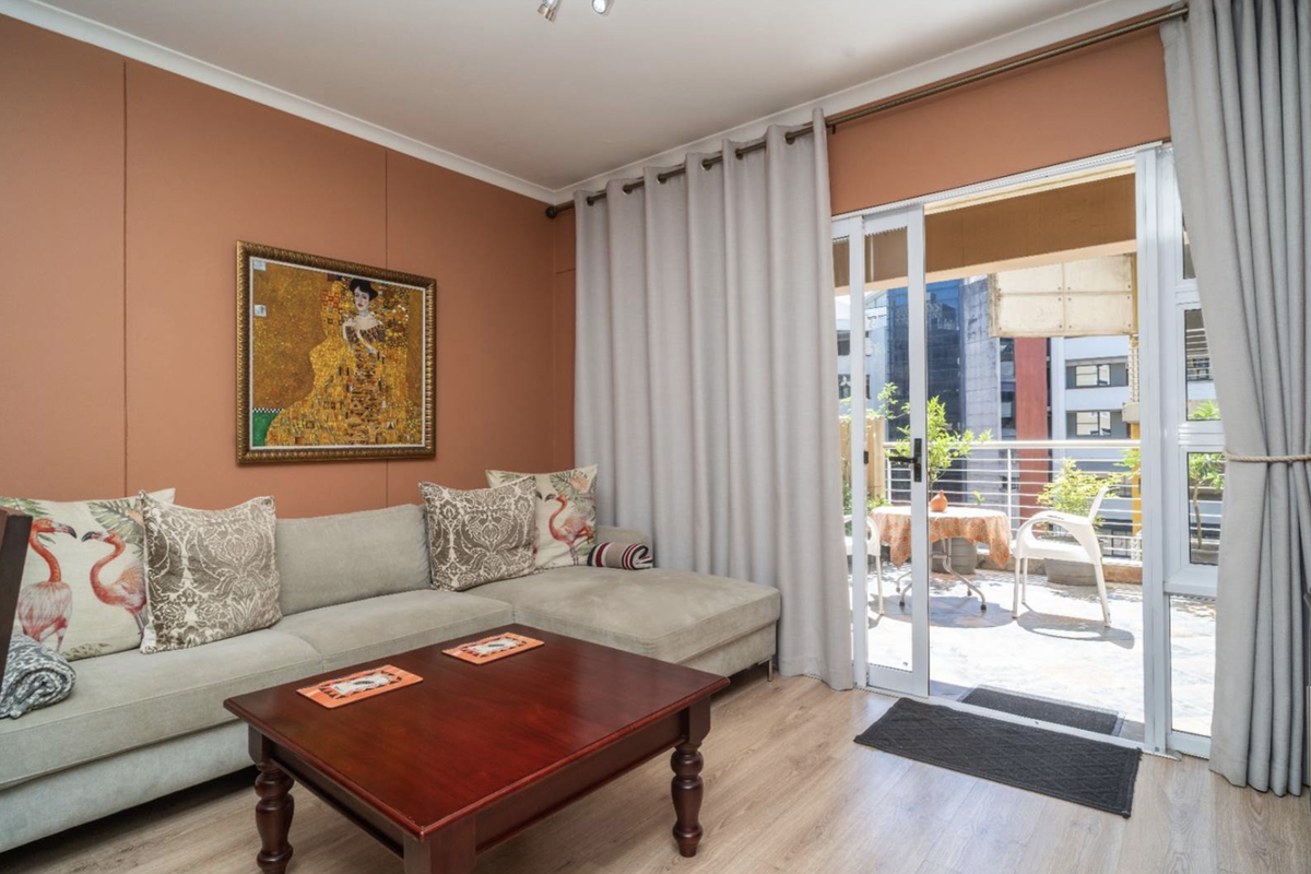A well-maintained living room featuring laminate flooring and a large sliding glass door providing direct access to an outdoor balcony area.