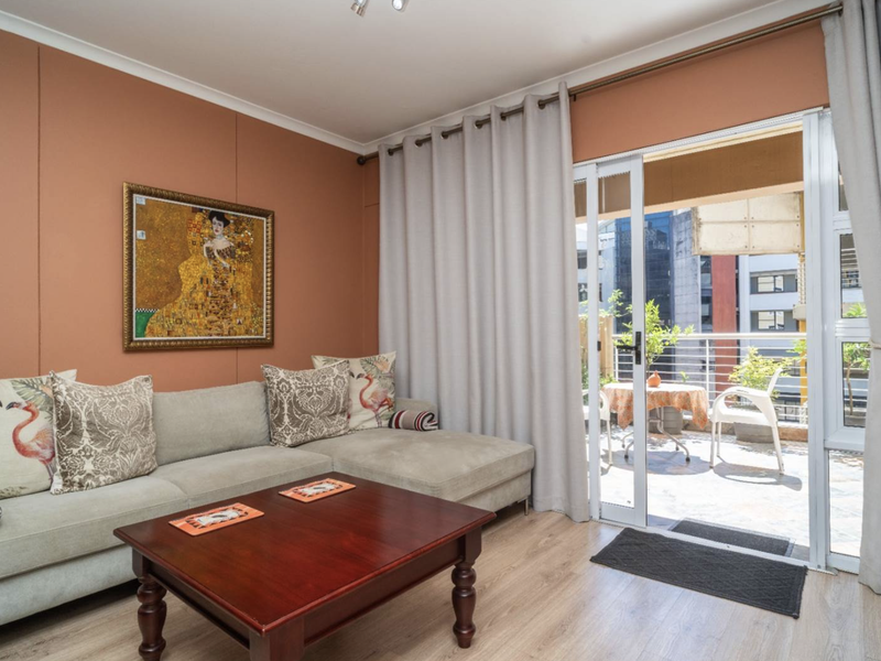 A well-maintained living room featuring laminate flooring and a large sliding glass door providing direct access to an outdoor balcony area.