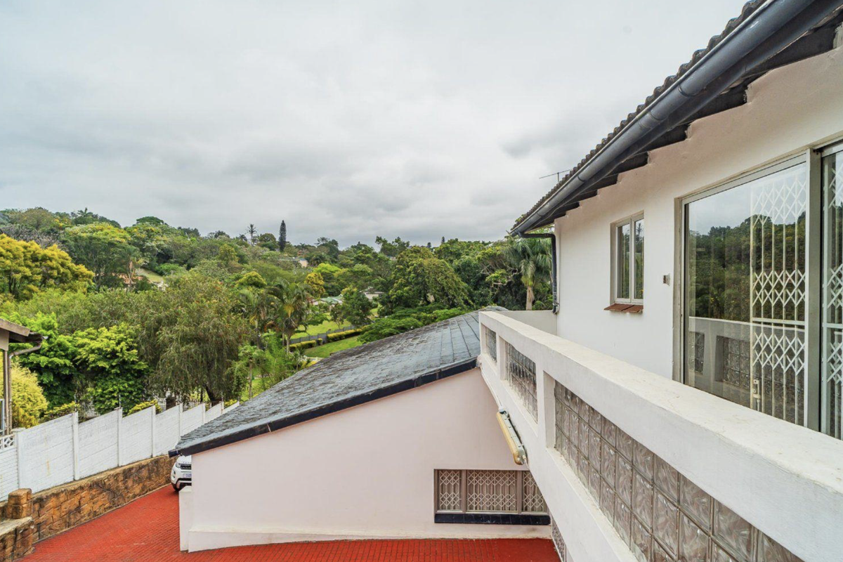 Rear exterior view of the property featuring a tiled roof, glass block wall detailing, and a paved driveway overlooking lush greenery.