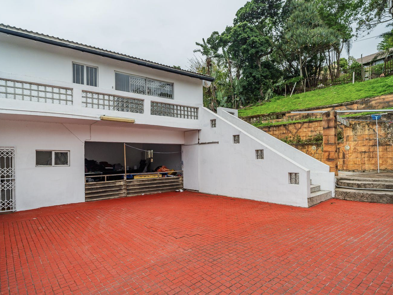 Rear exterior view featuring a large red paved courtyard, an external staircase leading to an upper balcony, and a lower-level garage area.