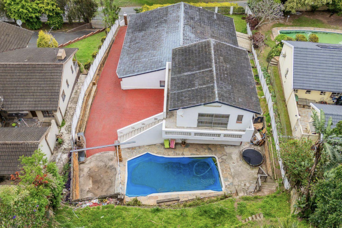 Aerial view of the property featuring a swimming pool, paved outdoor areas, and a tiled roof structure set within a residential neighborhood.