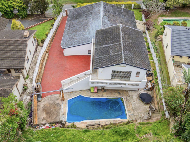 Aerial view of the property featuring a swimming pool, paved outdoor areas, and a tiled roof structure set within a residential neighborhood.