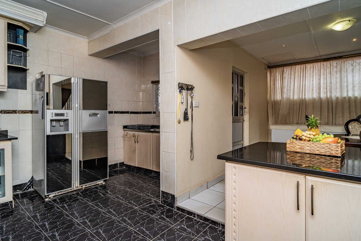 A functional kitchen featuring granite countertops, tiled walls, and dark tiled flooring, offering a practical layout with ample storage space.