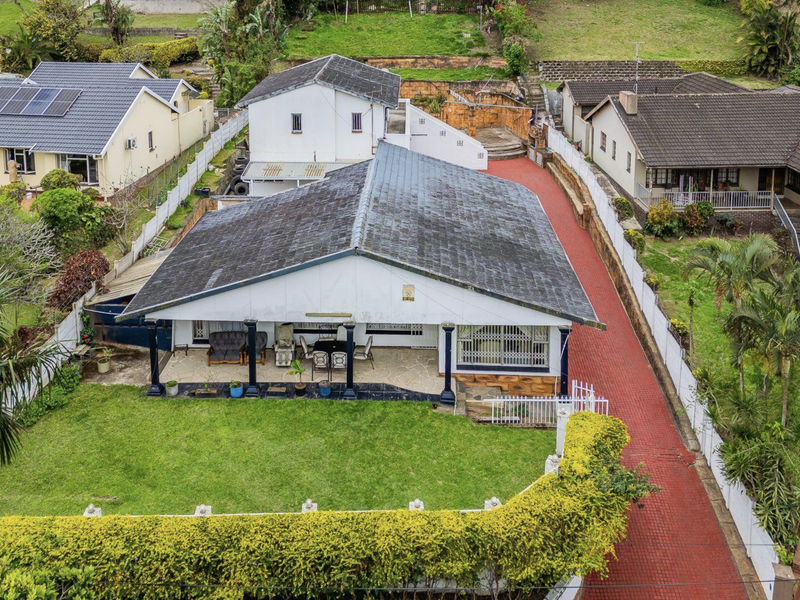 Aerial view of a residential property featuring a tiled roof, covered patio, expansive lawn, and a long paved driveway.