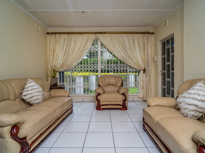 A well-lit living room featuring neutral tiled flooring, a large sliding door with security gate, and classic cornicing details.