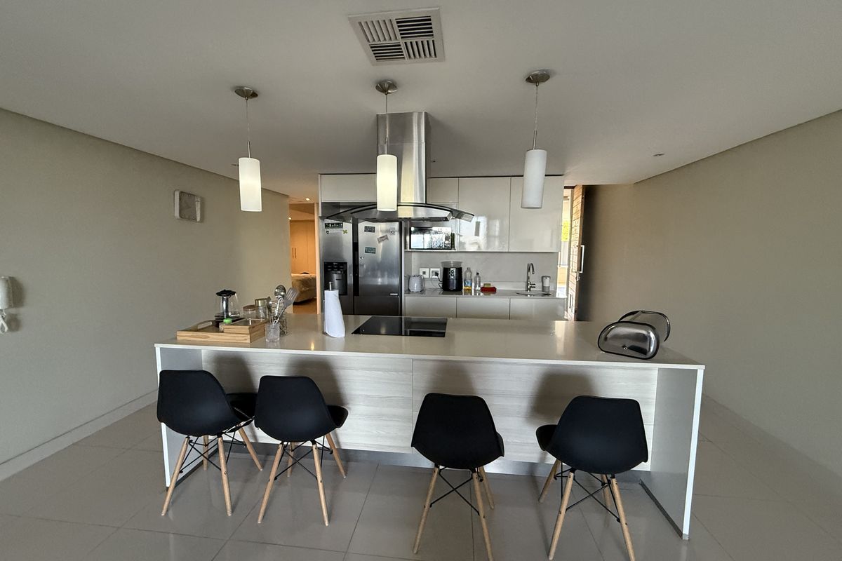 Modern kitchen featuring a central island with stone countertops, sleek cabinetry, stainless steel appliances, and contemporary pendant lighting.
