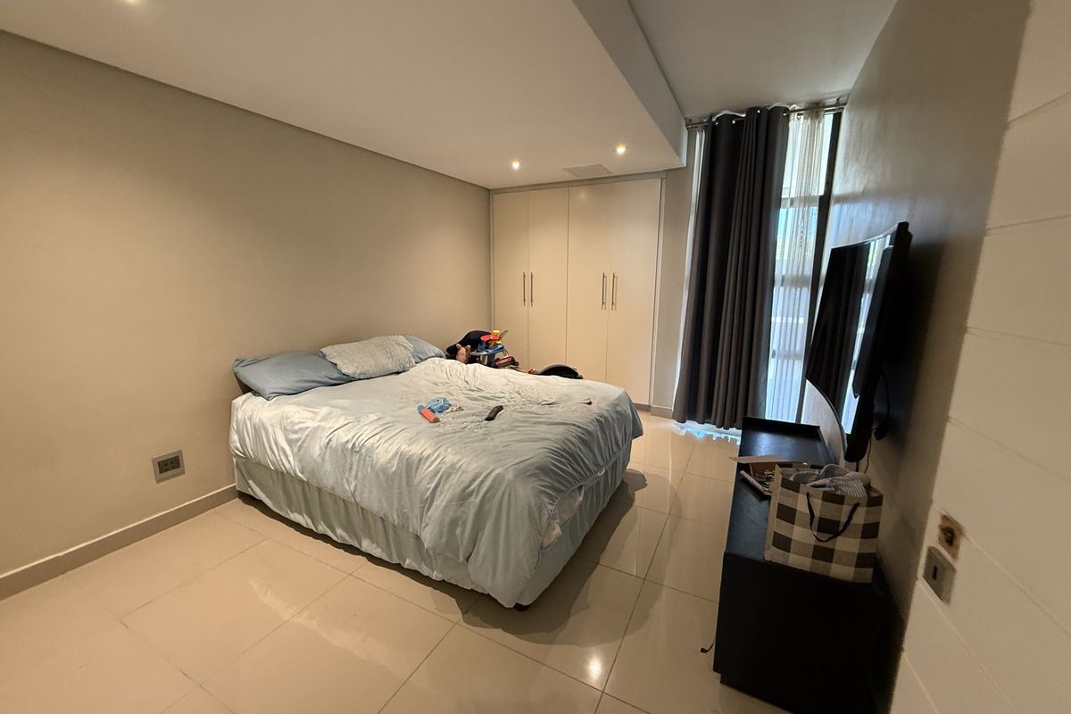 A well-proportioned bedroom featuring neutral tiled flooring, recessed downlighting, and ample built-in cupboard storage with large windows for natural light.