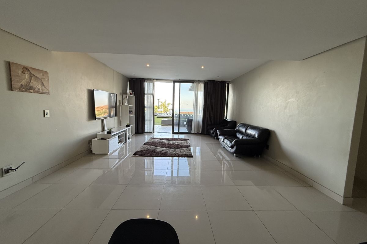 Spacious living room featuring large format porcelain floor tiles, recessed downlighting, and sliding glass doors providing access to an outdoor patio area.
