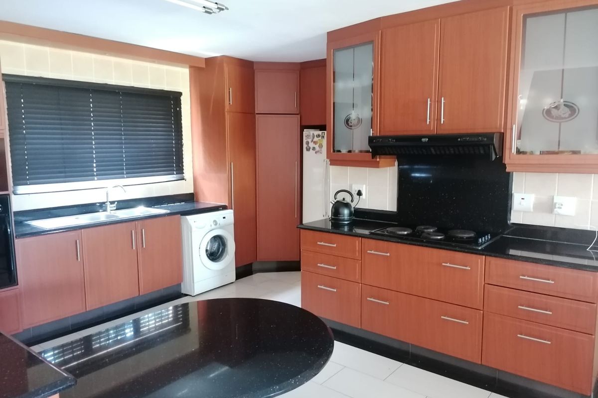 A functional kitchen featuring wood-finish cabinetry, black granite countertops, an integrated hob with extractor, and dedicated space for laundry appliances.