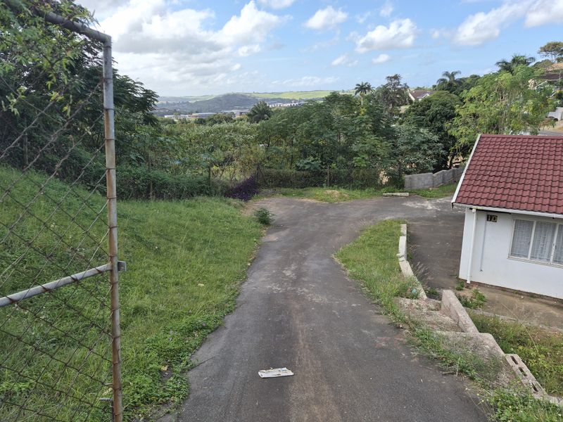 An exterior view of the property driveway and surrounding grounds, featuring a paved access path and partial view of the residential building structure.