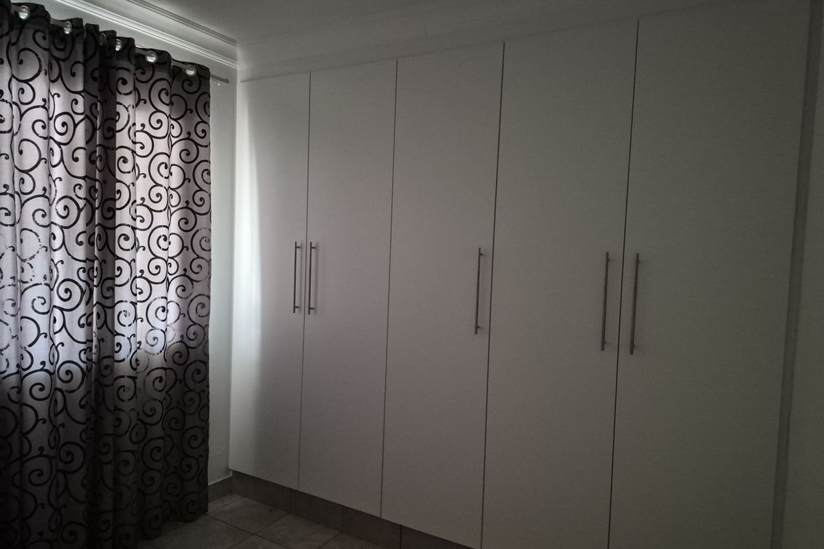 A bedroom featuring floor-to-ceiling built-in white cabinetry with modern handles and tiled flooring.