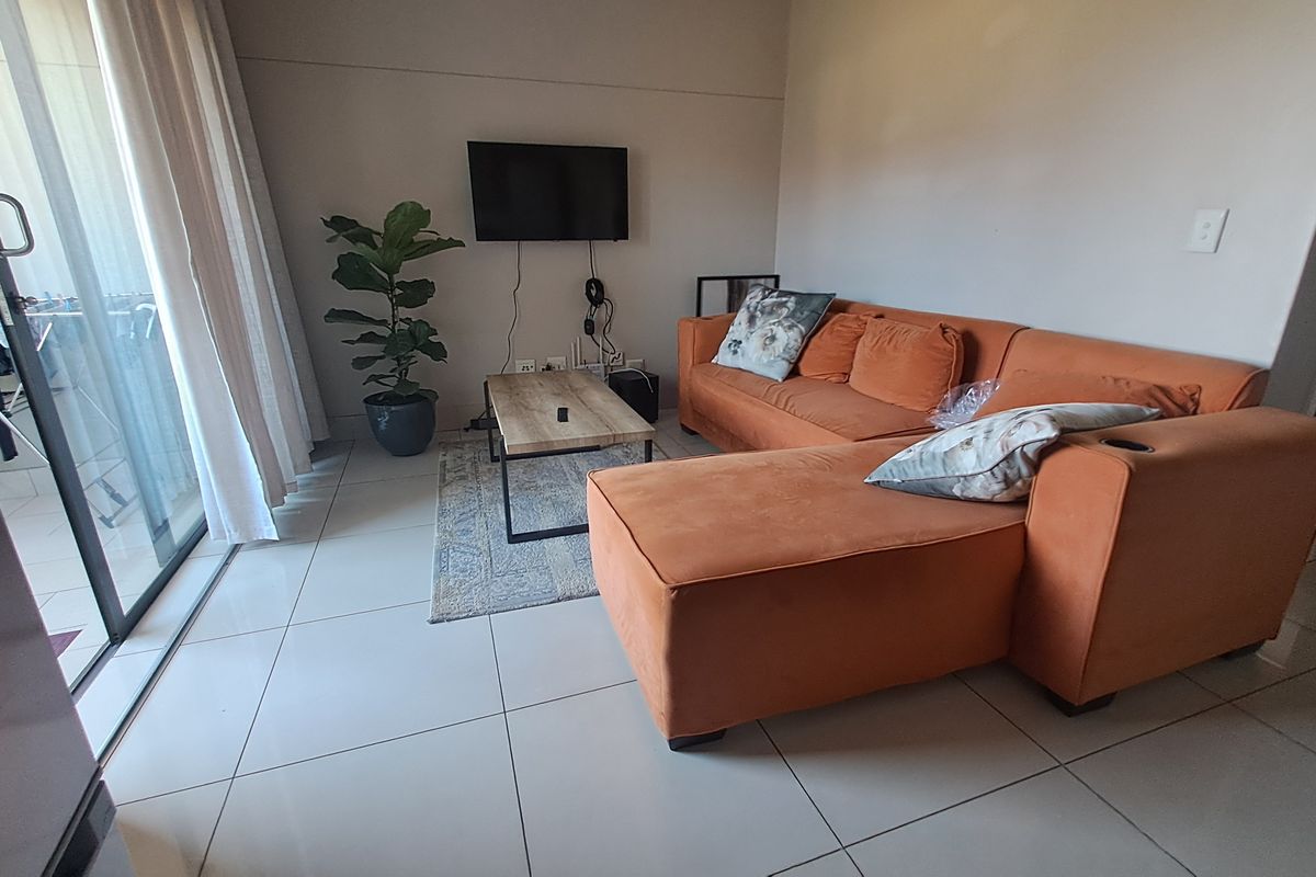 A bright living room featuring large sliding glass doors that open to a balcony, complemented by neutral floor tiles throughout the space.