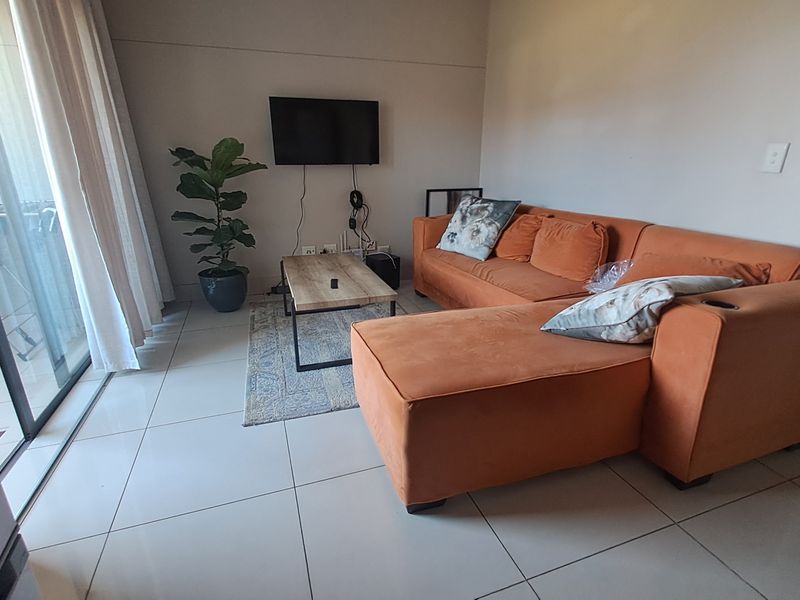 A bright living room featuring large sliding glass doors that open to a balcony, complemented by neutral floor tiles throughout the space.