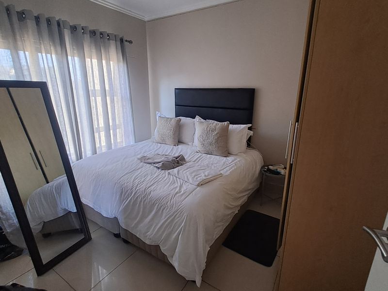 A well-lit bedroom featuring tiled flooring, a built-in wardrobe, and large windows with curtains, providing a comfortable and functional living space.