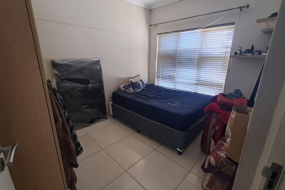 A compact bedroom featuring tiled flooring and a large window with fitted blinds, providing natural light to the space.