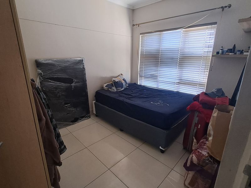 A compact bedroom featuring tiled flooring and a large window with fitted blinds, providing natural light to the space.
