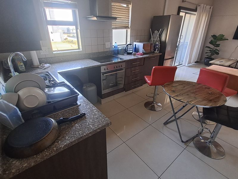 Open-plan kitchen and living area featuring tiled flooring, built-in cabinetry, integrated oven, hob, and extractor fan, with direct access to a balcony.