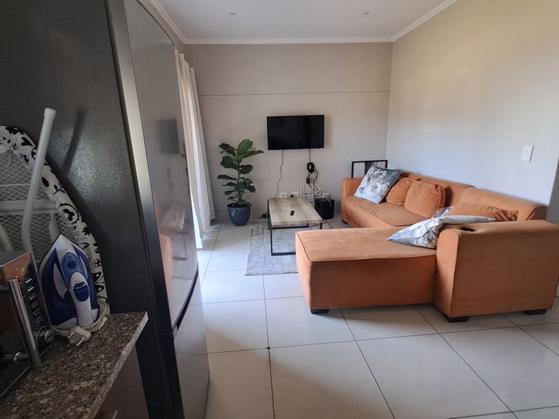 Open plan living area featuring tiled flooring and a wall-mounted television, seamlessly connecting to the kitchen space.