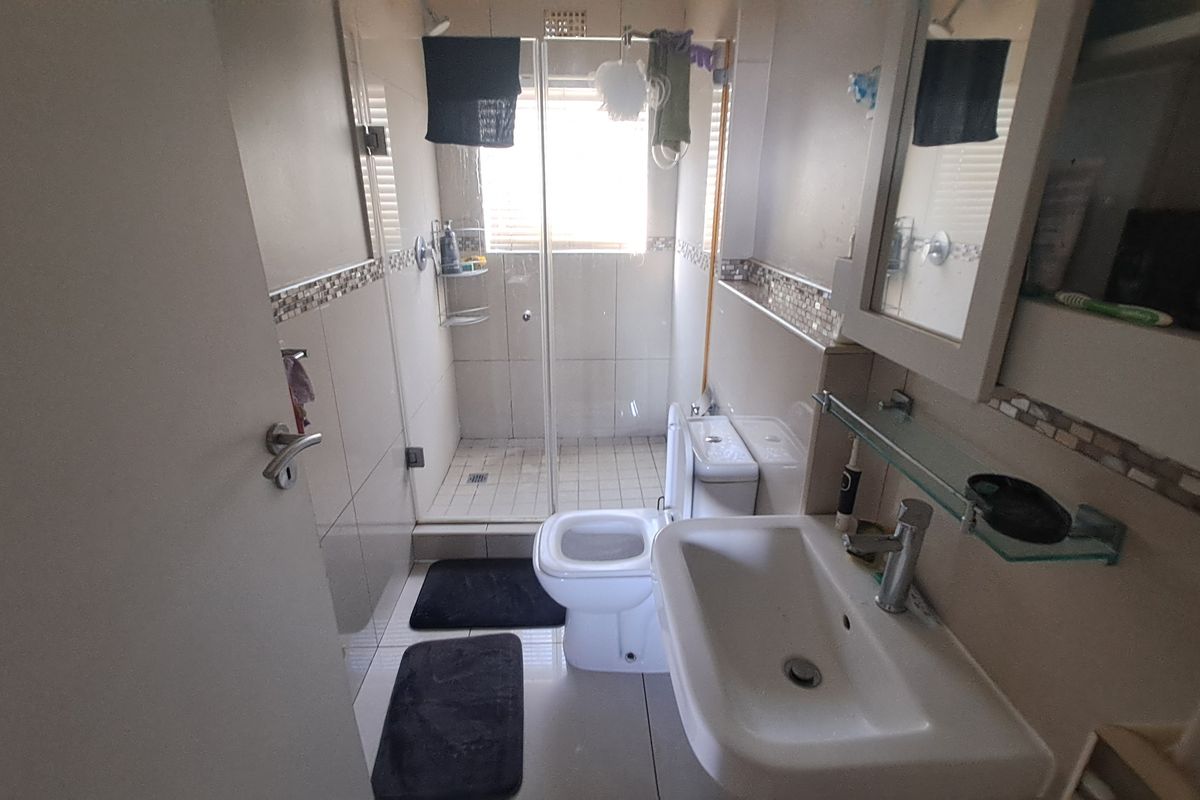 Compact bathroom featuring a glass-enclosed shower, ceramic basin, and toilet with neutral wall tiling and mosaic accents.