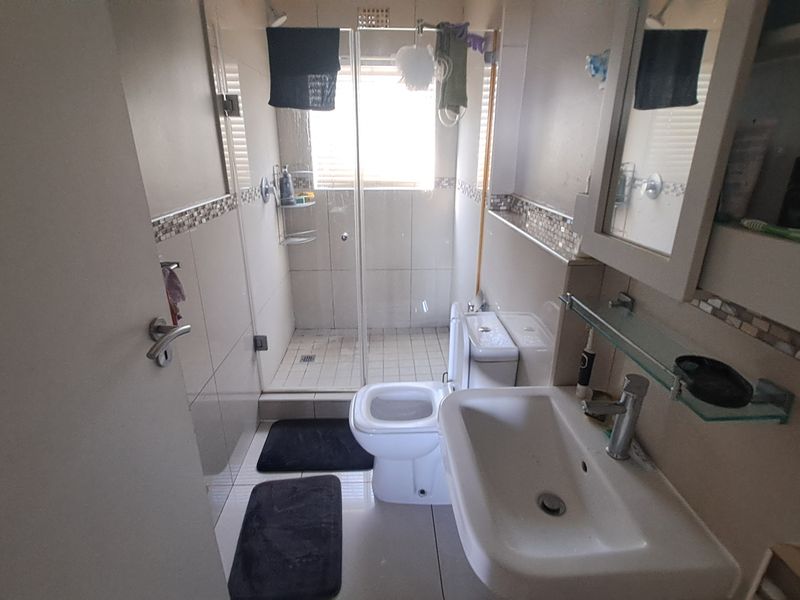Compact bathroom featuring a glass-enclosed shower, ceramic basin, and toilet with neutral wall tiling and mosaic accents.