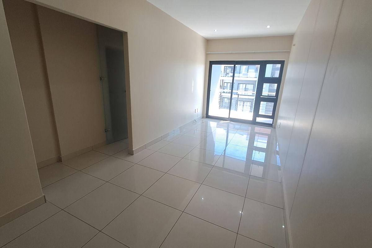 A bright, empty living area featuring polished tile flooring and a large sliding glass door that provides natural light and access to the exterior.