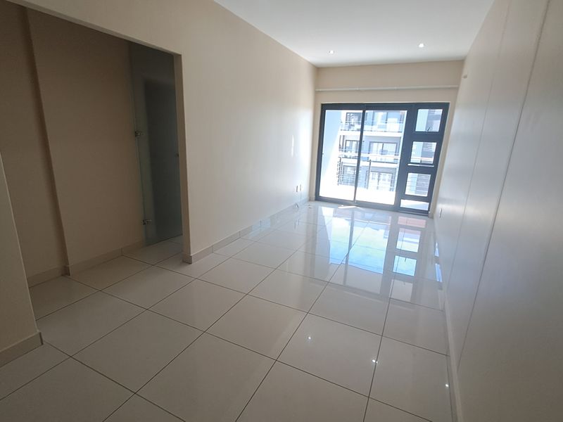 A bright, empty living area featuring polished tile flooring and a large sliding glass door that provides natural light and access to the exterior.