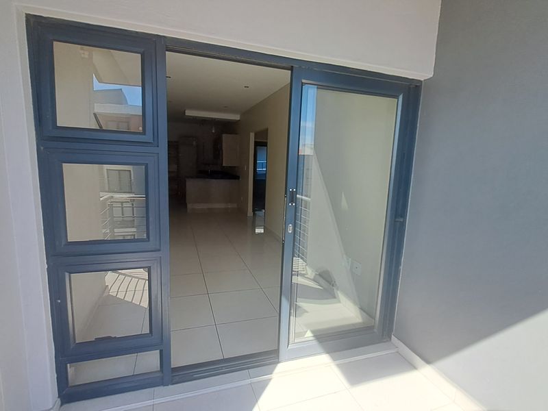 A clean, modern balcony featuring tiled flooring and a large sliding glass door providing seamless access to the open-plan interior living space.