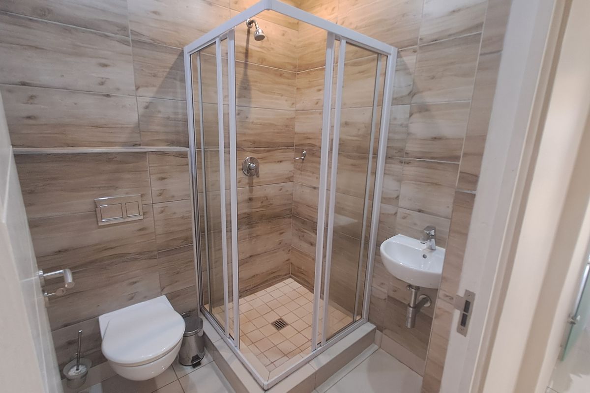 Modern bathroom featuring a corner shower enclosure, wall-mounted toilet with concealed cistern, and a compact wall-mounted basin with wood-look tiled walls.