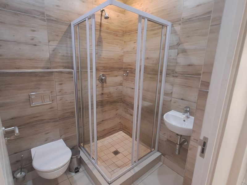 Modern bathroom featuring a corner shower enclosure, wall-mounted toilet with concealed cistern, and a compact wall-mounted basin with wood-look tiled walls.